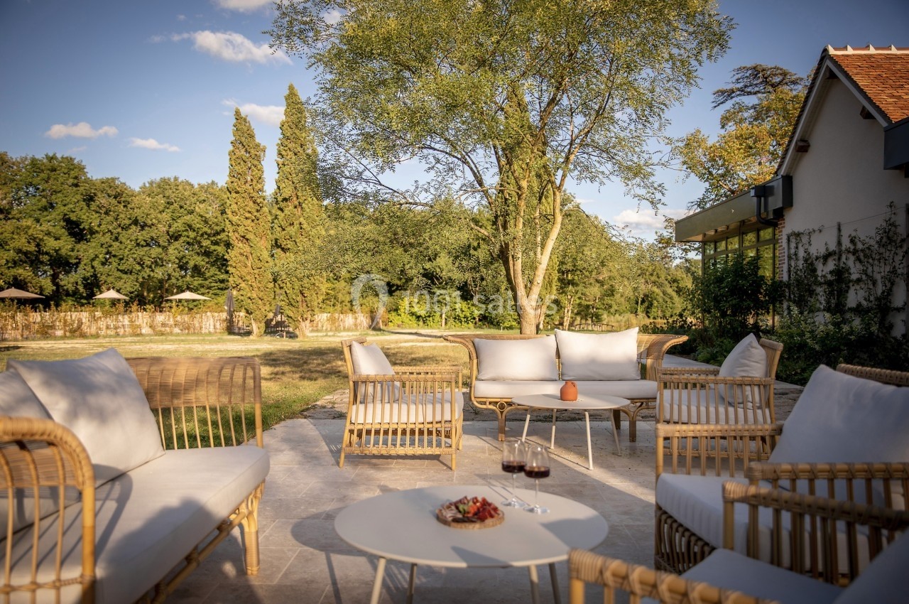 Mobilier de jardin en rotin sur une terrasse ensoleillée, entourée d'arbres et d'une pelouse.