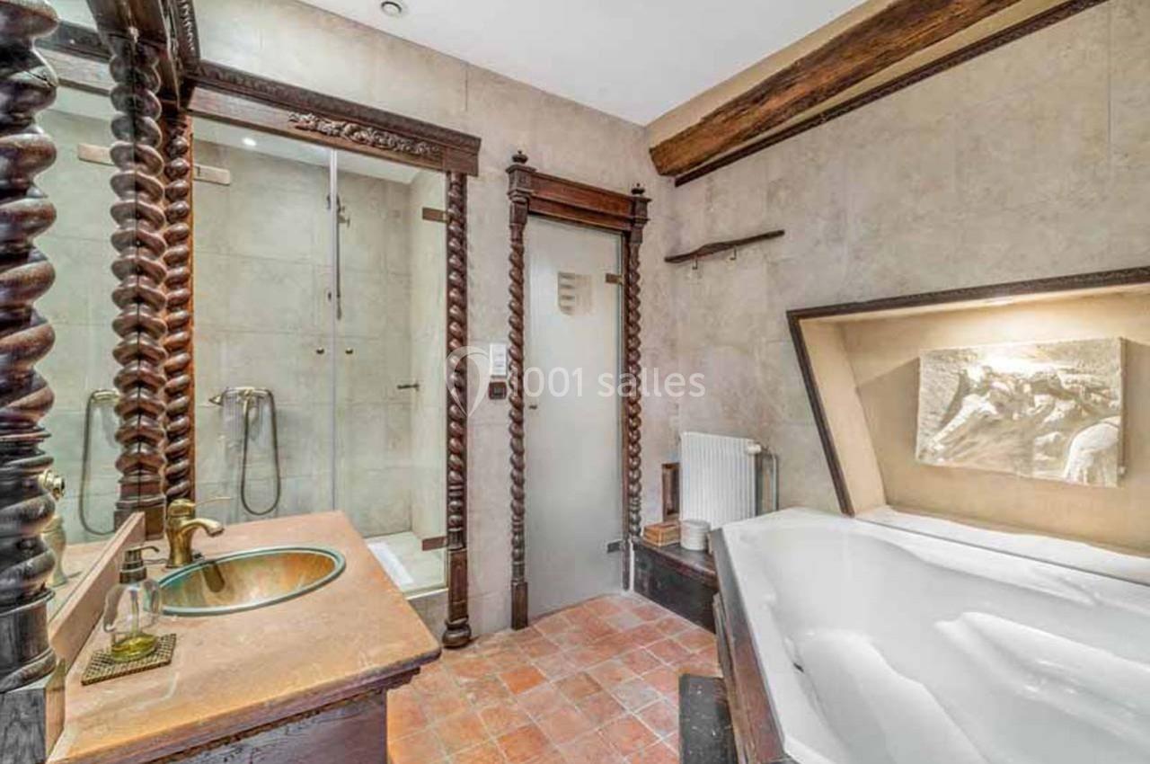 Salle de bain avec baignoire d'angle, douche vitrée, lavabo sur plan en bois et poutres apparentes.