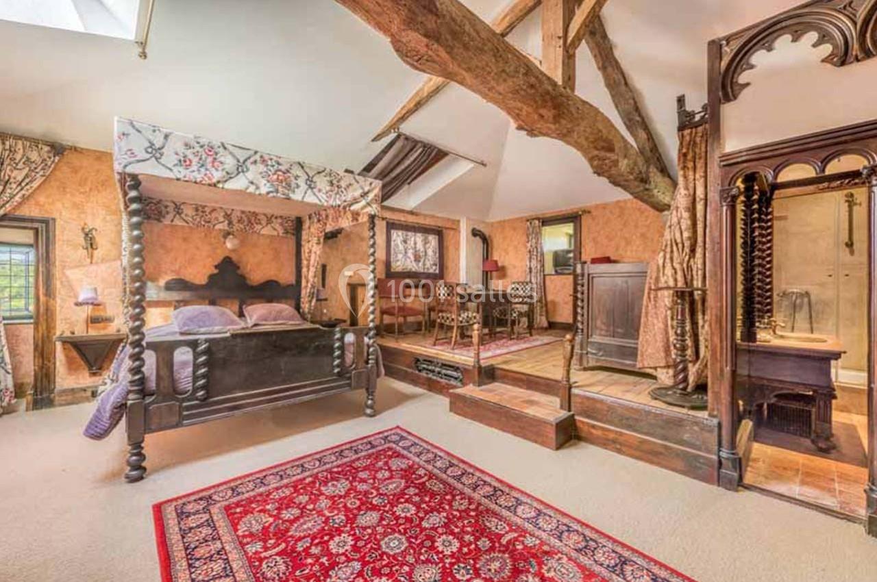 Chambre rustique avec lit à baldaquin, poutres apparentes, tapis rouge et mobilier en bois ancien.