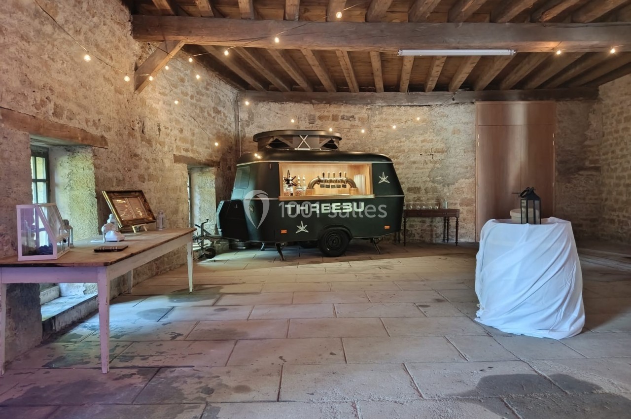 Bar mobile vert dans une salle en pierre avec poutres apparentes, éclairée par des guirlandes lumineuses.