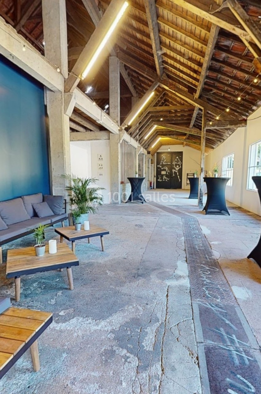 Espace intérieur industriel avec plafond en bois, tables basses, plantes et tables hautes pour événement.