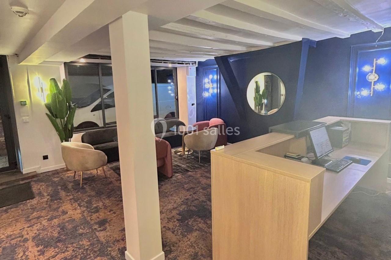 Espace d'accueil moderne avec comptoir en bois, fauteuils colorés, miroir rond et éclairage design.