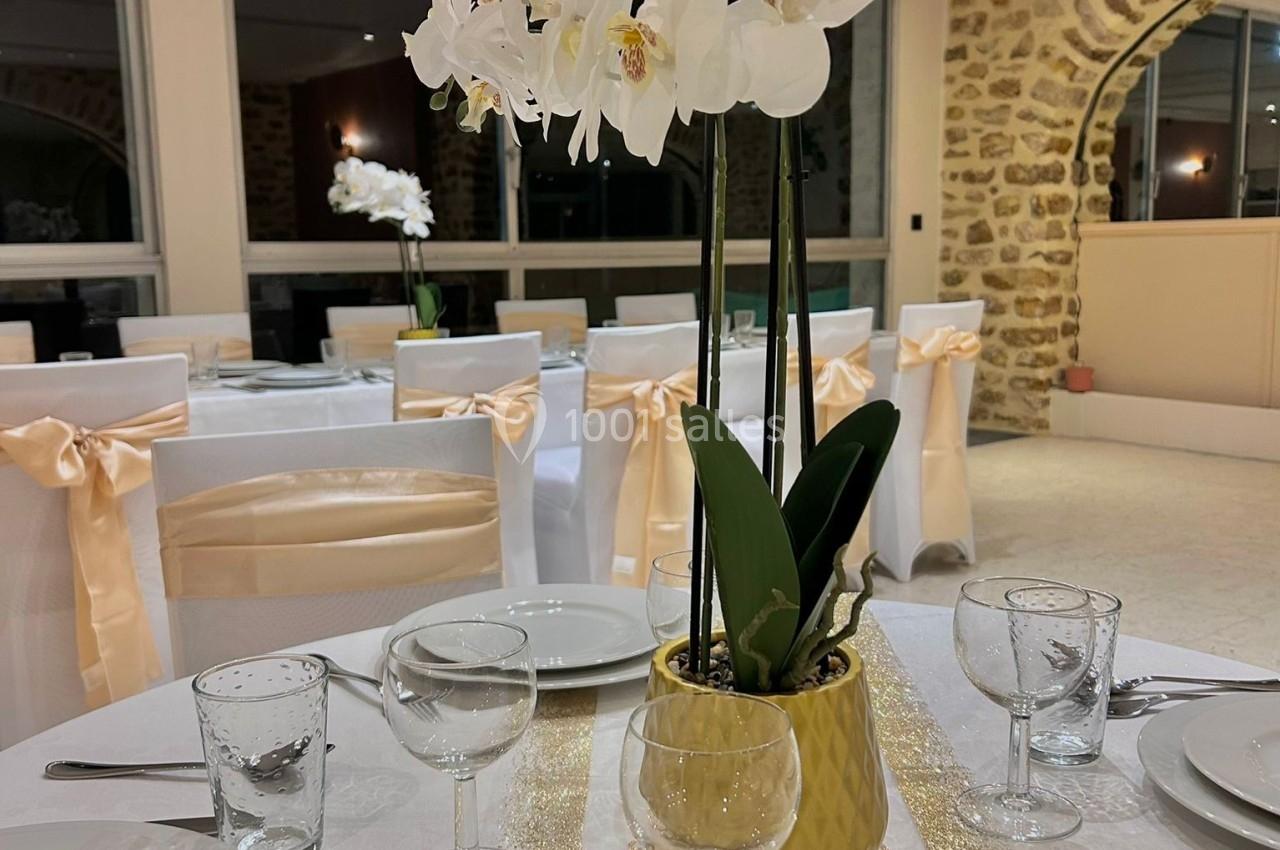 Orchidée blanche dans un vase doré au centre d'une table décorée pour un événement, avec nappes et rubans élégants.