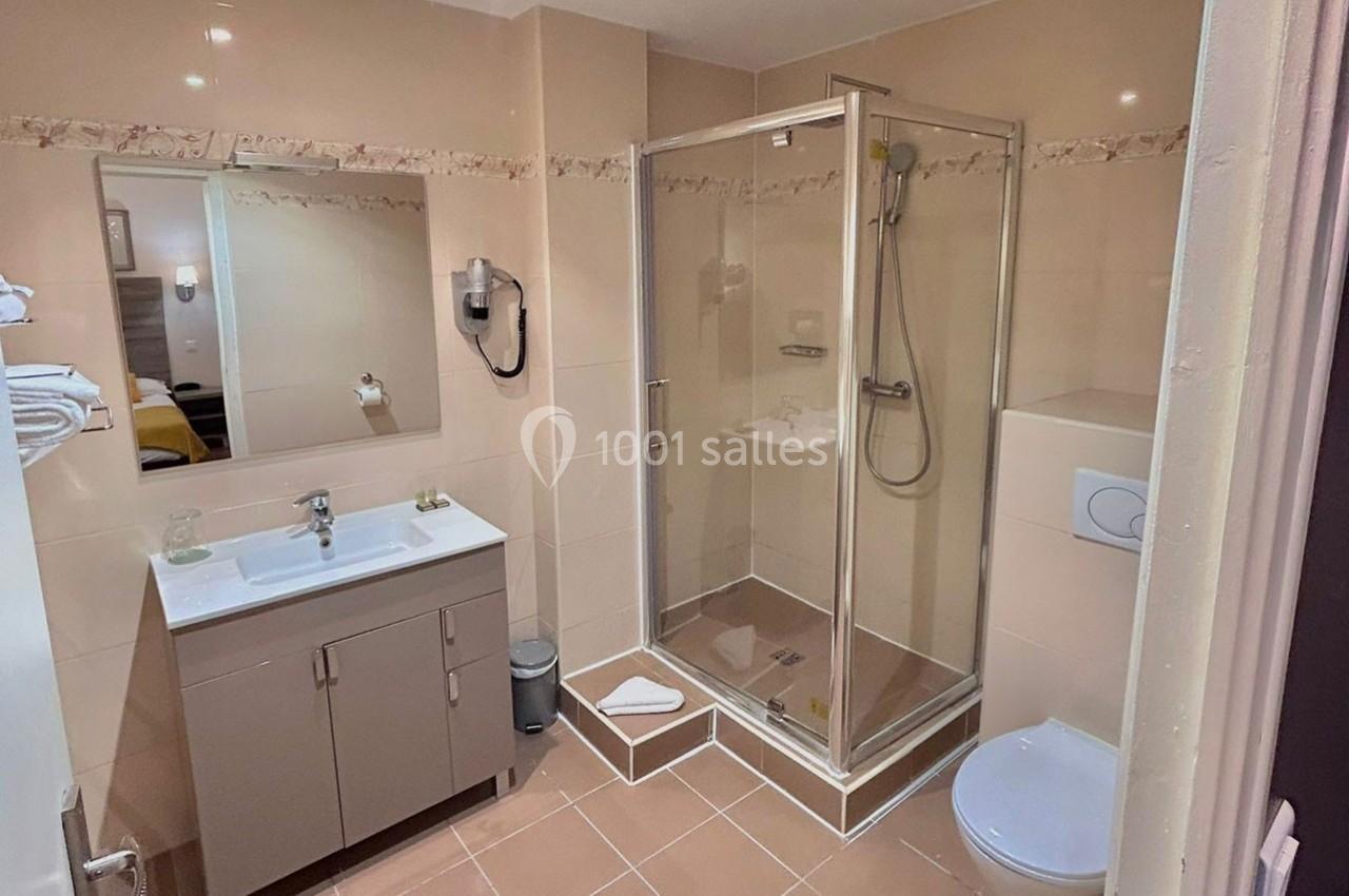 Salle de bain avec douche vitrée, lavabo avec meuble, miroir, sèche-cheveux mural et toilettes.