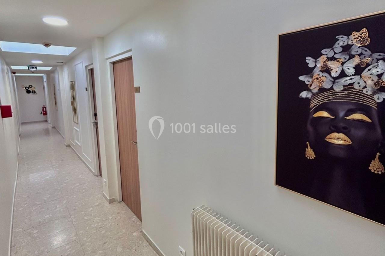 Couloir lumineux avec murs blancs, portes en bois, tableau représentant un visage décoré de papillons et éléments dorés.