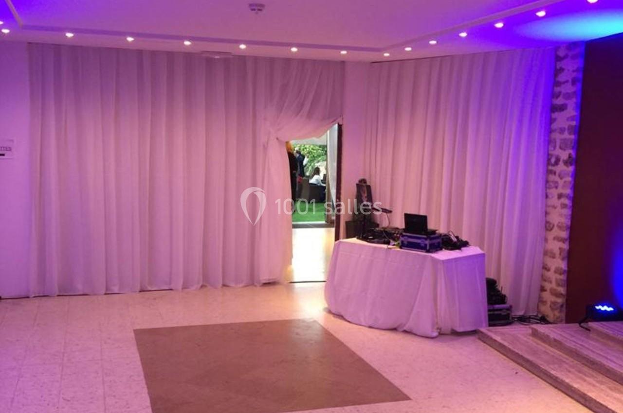 Salle avec rideaux blancs, éclairage tamisé, table équipée de matériel audio et porte ouverte sur un espace extérieur.