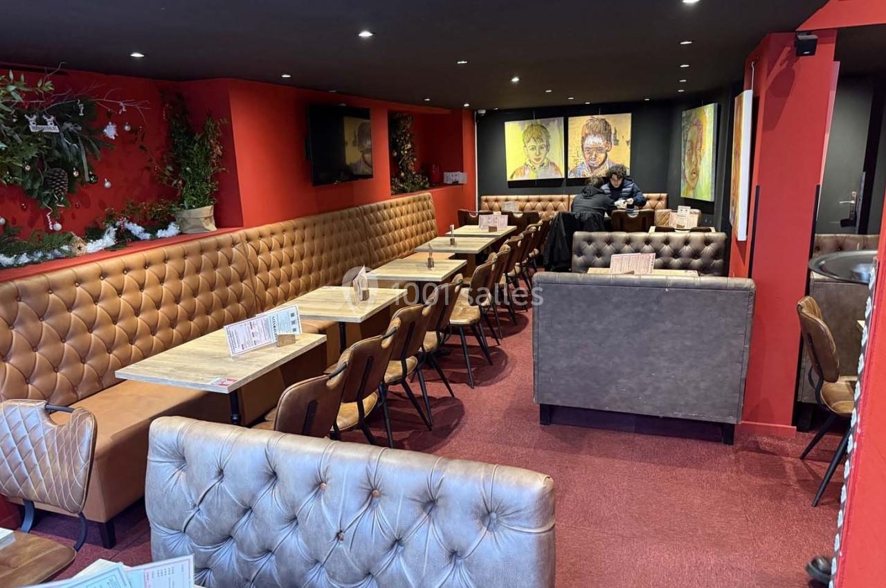 Salle de restaurant avec banquettes en cuir, tables en bois, murs rouges et décorations murales colorées.