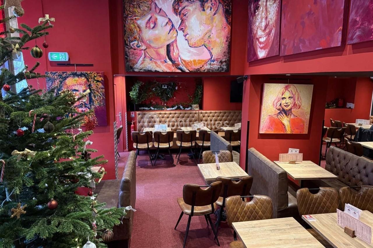 Intérieur d'un restaurant avec murs rouges, tableaux colorés, tables en bois et un sapin de Noël décoré.