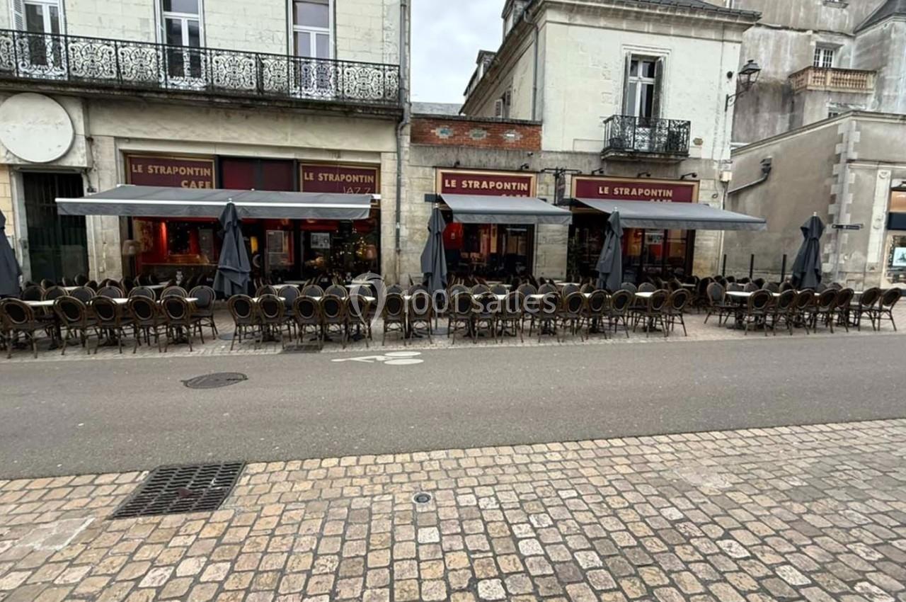 Terrasse vide d'un café-restaurant avec des chaises alignées, située devant des bâtiments en pierre.
