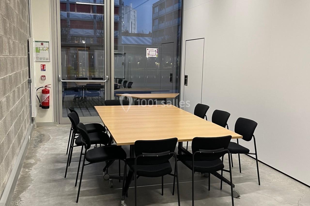 Salle de réunion avec une table rectangulaire en bois entourée de chaises noires, située près d'une grande baie vitrée.
