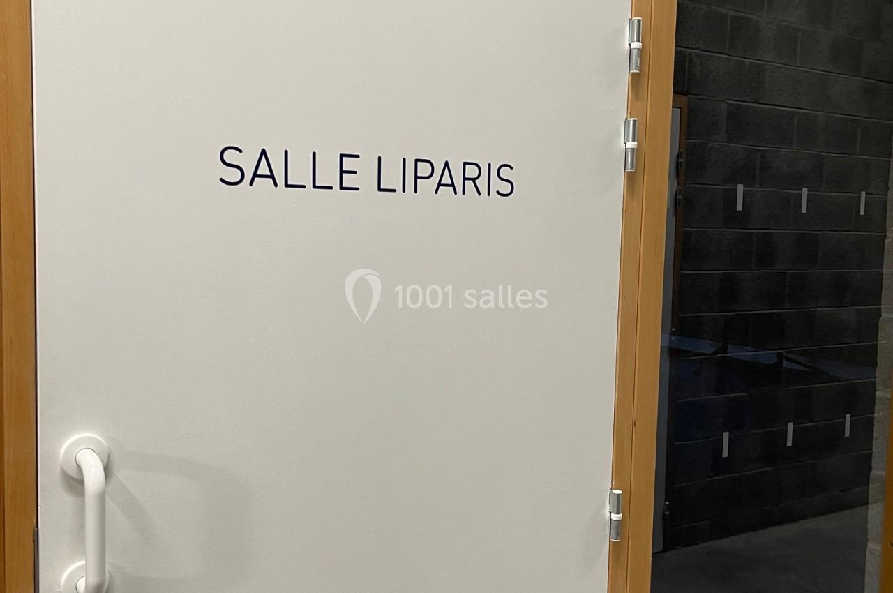 Porte blanche avec l'inscription ’Salle Liparis’, entourée d'un cadre en bois et située dans un mur en béton.