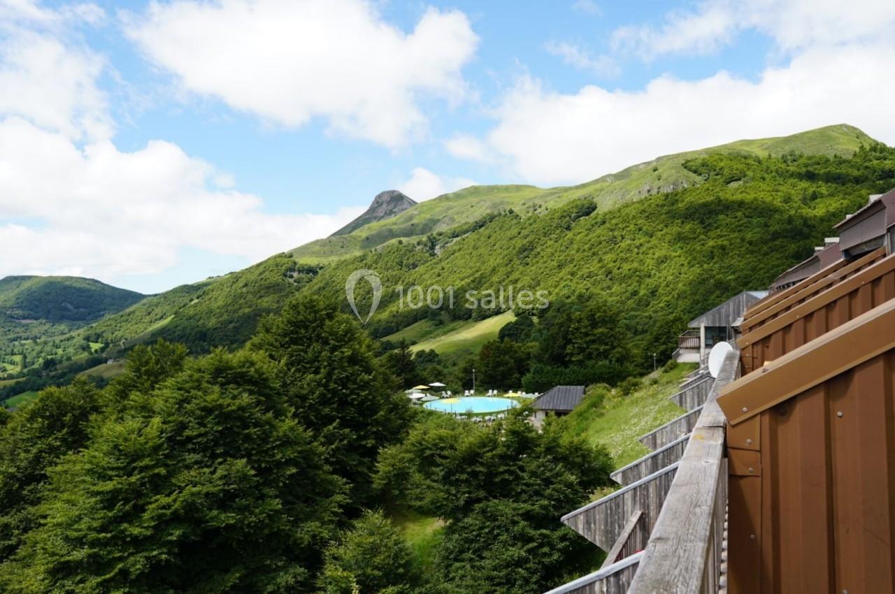 Vue sur des collines verdoyantes avec une piscine entourée d'arbres, prise depuis un balcon en bois.