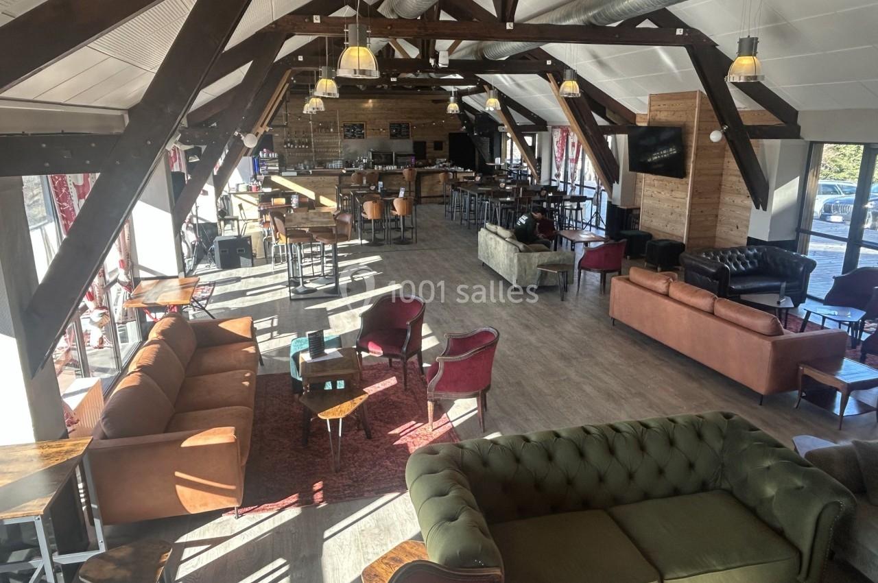Espace intérieur lumineux avec poutres apparentes, mobilier varié et coin bar au fond.