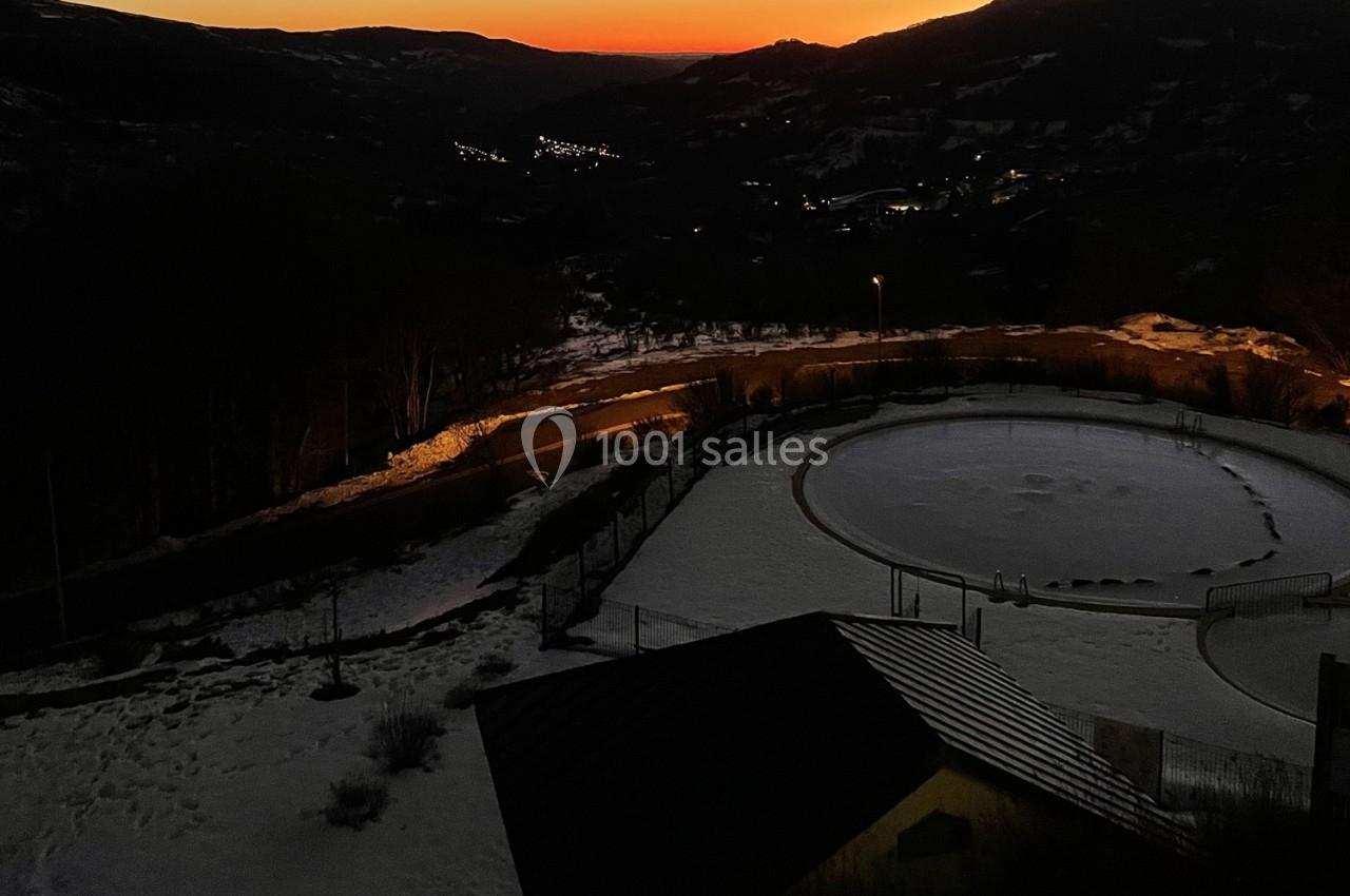 Vue nocturne d'un paysage enneigé avec une piste circulaire éclairée et un ciel rougeoyant à l'horizon.