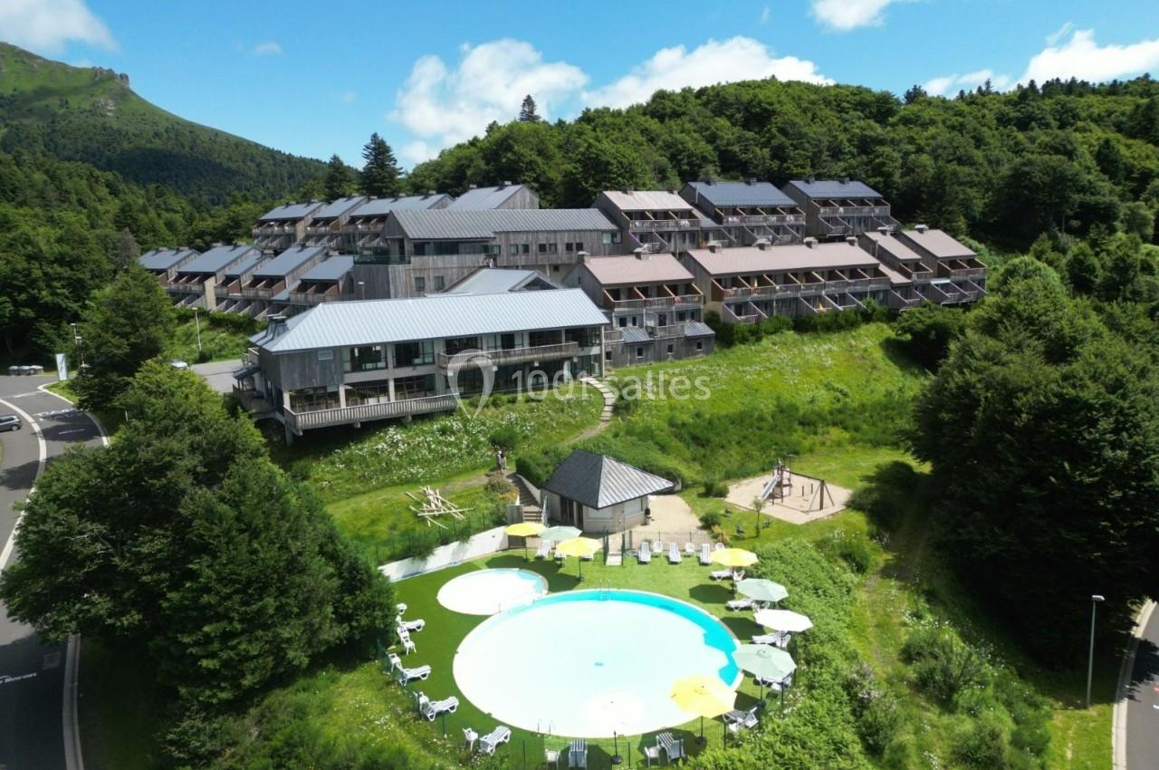 Vue aérienne d'un complexe hôtelier entouré de verdure avec une piscine extérieure et des parasols.