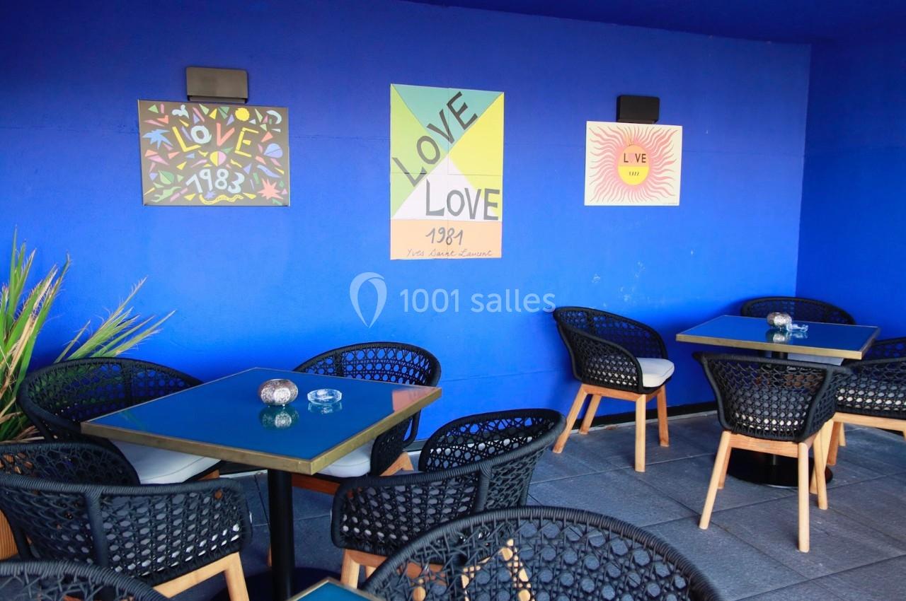 Terrasse avec tables et chaises noires, murs bleus décorés d'affiches colorées sur le thème de l'amour.
