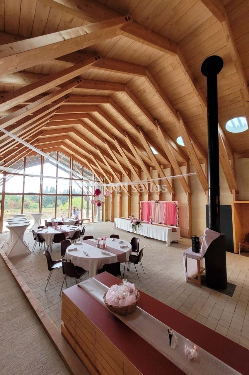 Salle en bois avec charpente apparente, tables rondes dressées et décorations pour un événement.