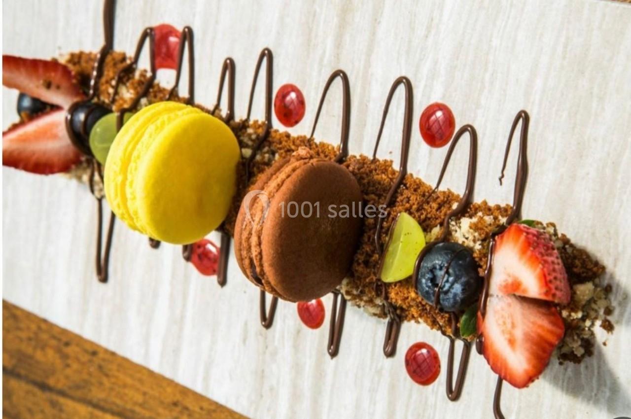 Dessert composé de macarons, fruits frais, miettes de biscuit et filet de chocolat sur une assiette claire.