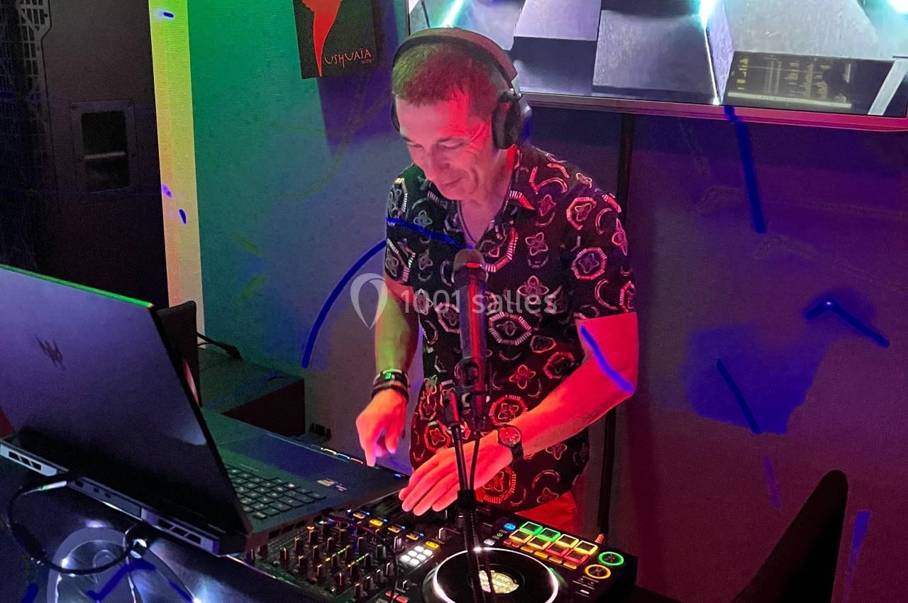 Un DJ mixe de la musique sur une console dans une ambiance lumineuse avec un écran affichant des visuels en arrière-plan.