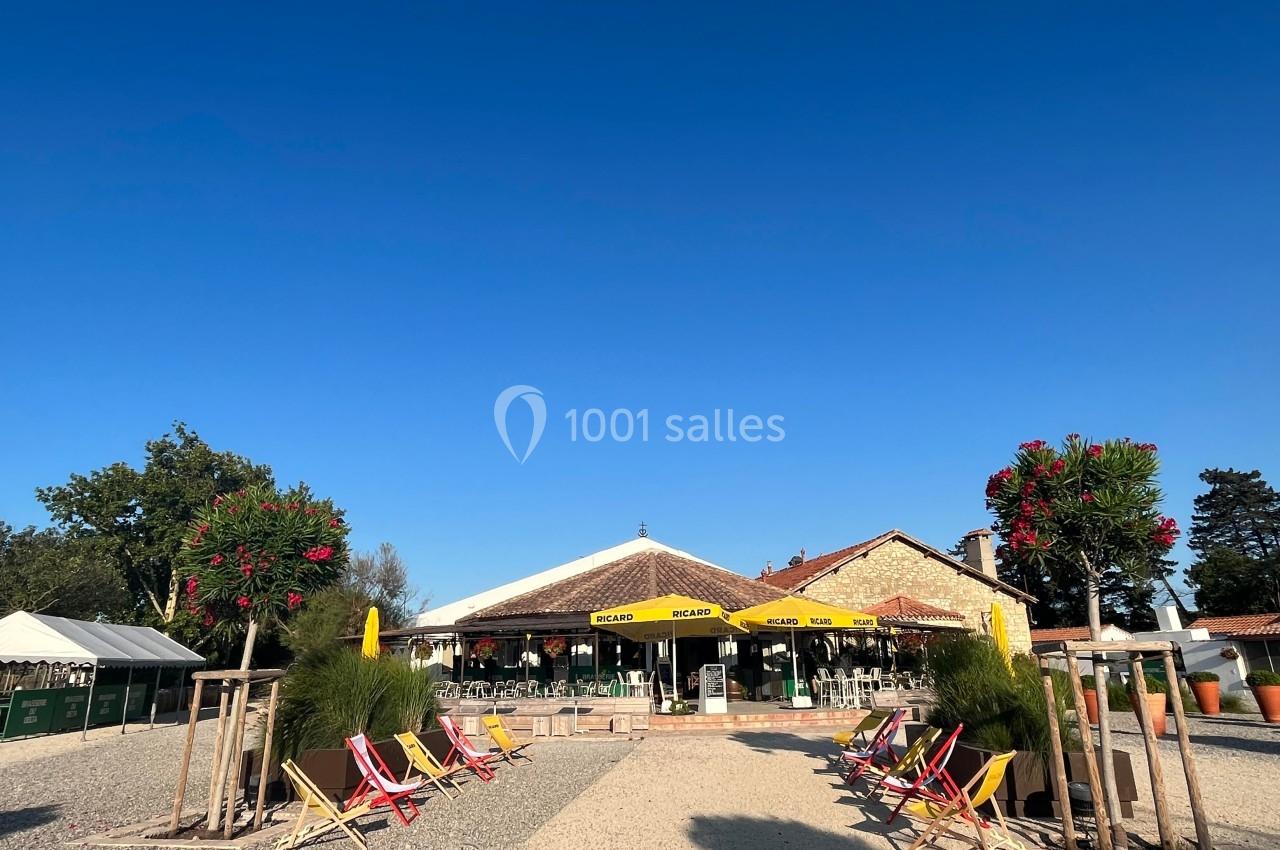 Terrasse d'un restaurant avec parasols jaunes, chaises longues colorées et arbres fleuris sous un ciel bleu.