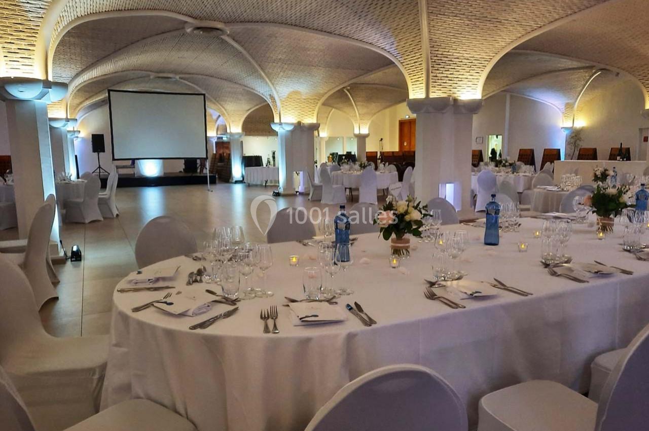 Salle de réception élégante avec tables dressées, décorations florales et écran de projection en arrière-plan.