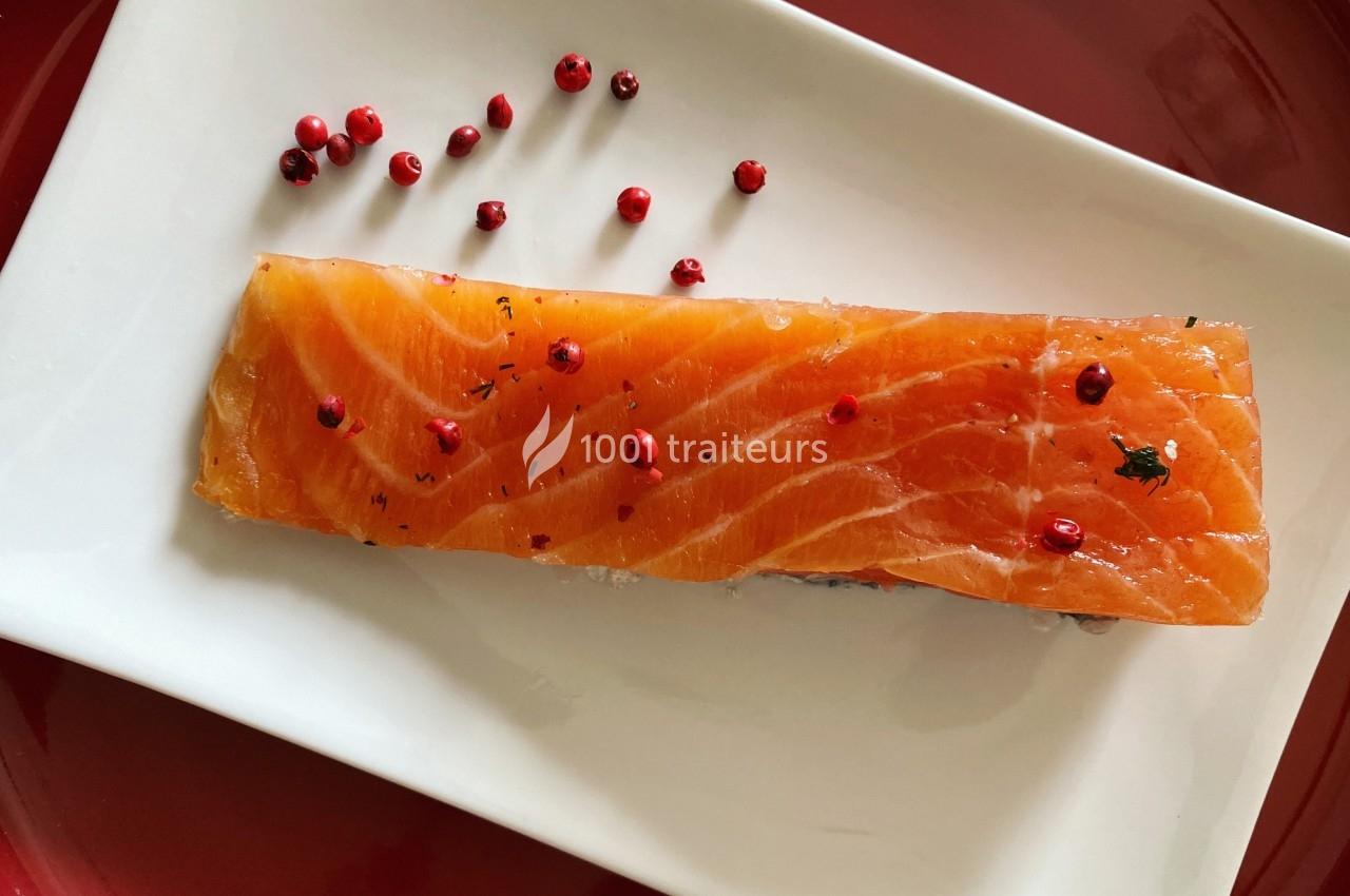 Tranche de saumon cru sur une assiette blanche, décorée de baies roses et d'herbes.