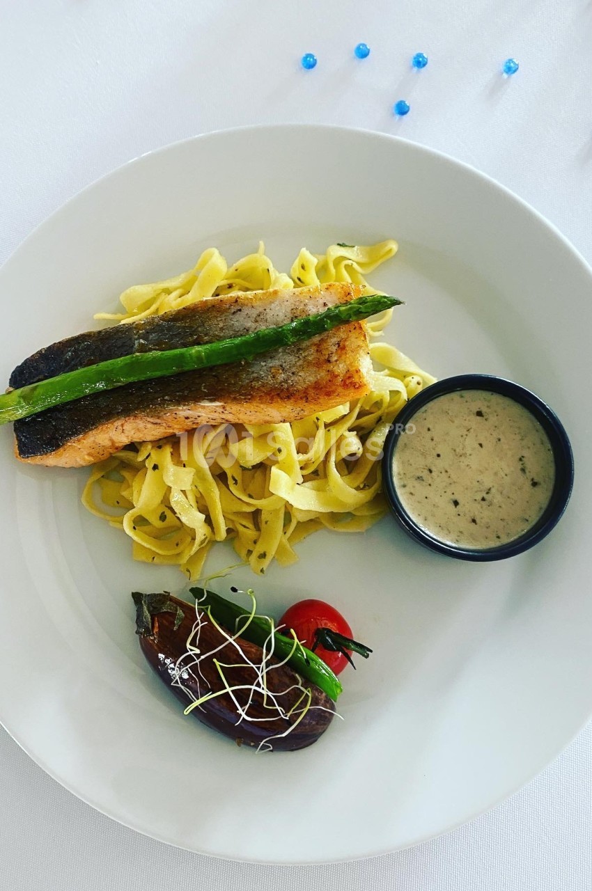 Assiette avec filet de saumon grillé sur tagliatelles, sauce en ramequin, tomate cerise et aubergine garnie.