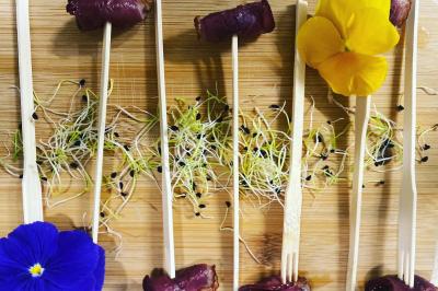 Deux hommes cuisinent des aliments sur un grand barbecue en plein air, éclairé par les flammes, à la tombée de la nuit.