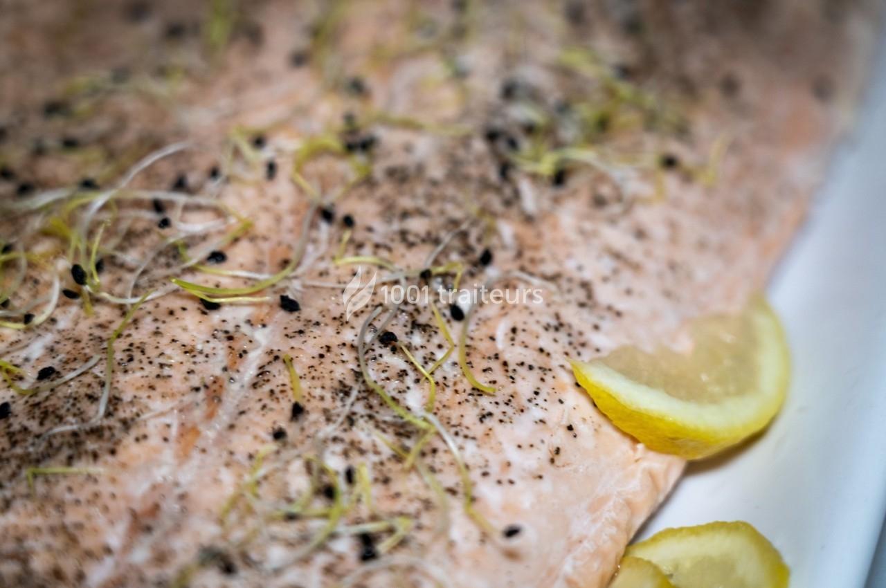 Filet de saumon cru assaisonné de poivre et garni de jeunes pousses, accompagné de quartiers de citron.