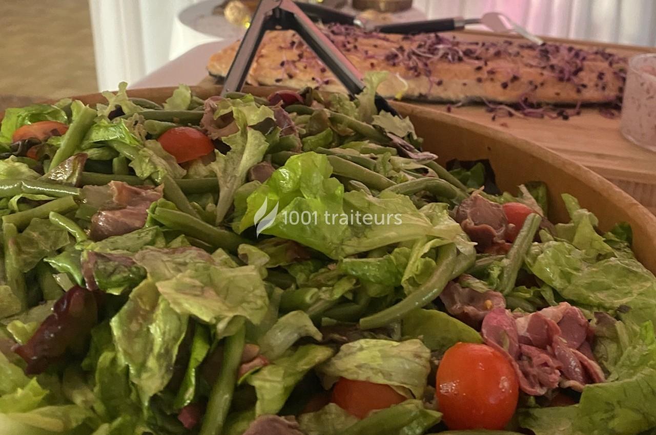 Salade composée de feuilles vertes, haricots verts, tomates cerises et morceaux de viande, avec un pain en arrière-plan.