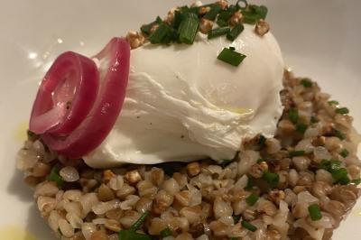 Deux hommes cuisinent des aliments sur un grand barbecue en plein air, éclairé par les flammes, à la tombée de la nuit.