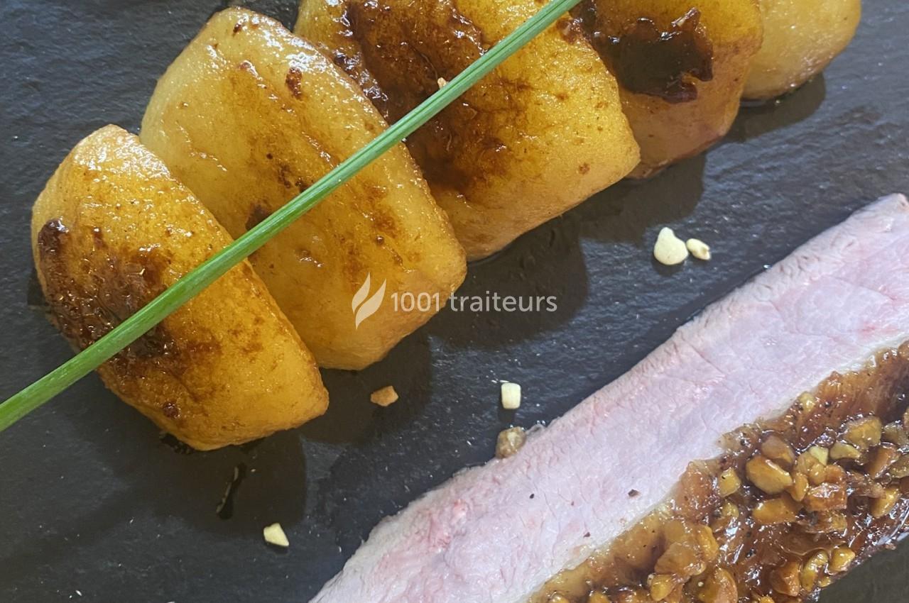 Tranche de viande accompagnée de pommes de terre dorées et d'une sauce aux éclats de noix, sur une assiette noire.
