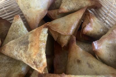 Deux hommes cuisinent des aliments sur un grand barbecue en plein air, éclairé par les flammes, à la tombée de la nuit.