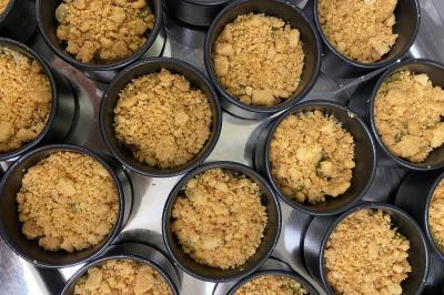 Deux hommes cuisinent des aliments sur un grand barbecue en plein air, éclairé par les flammes, à la tombée de la nuit.