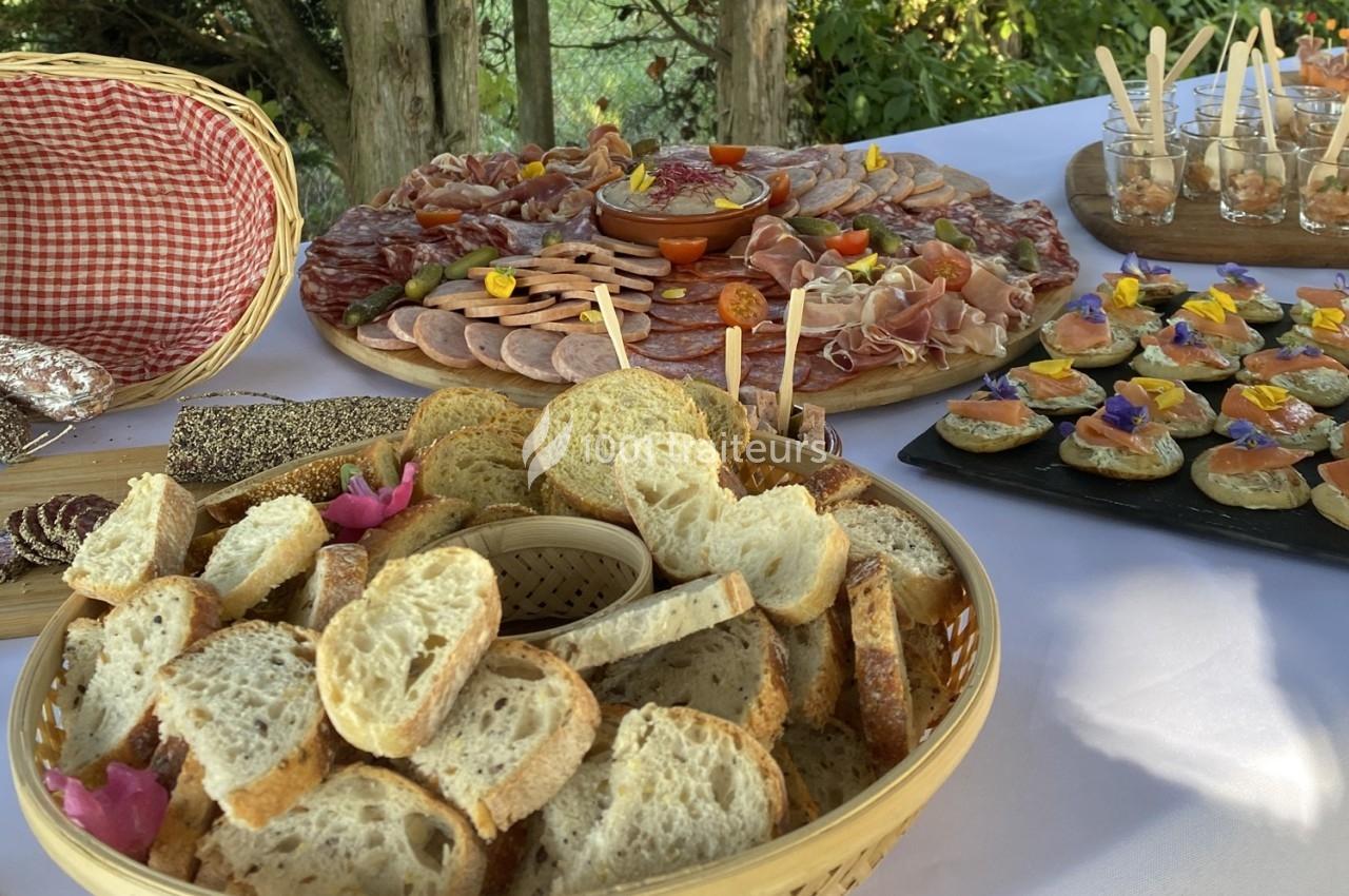 Plateau de pain tranché, charcuteries, verrines et toasts disposés sur une table pour un buffet en extérieur.
