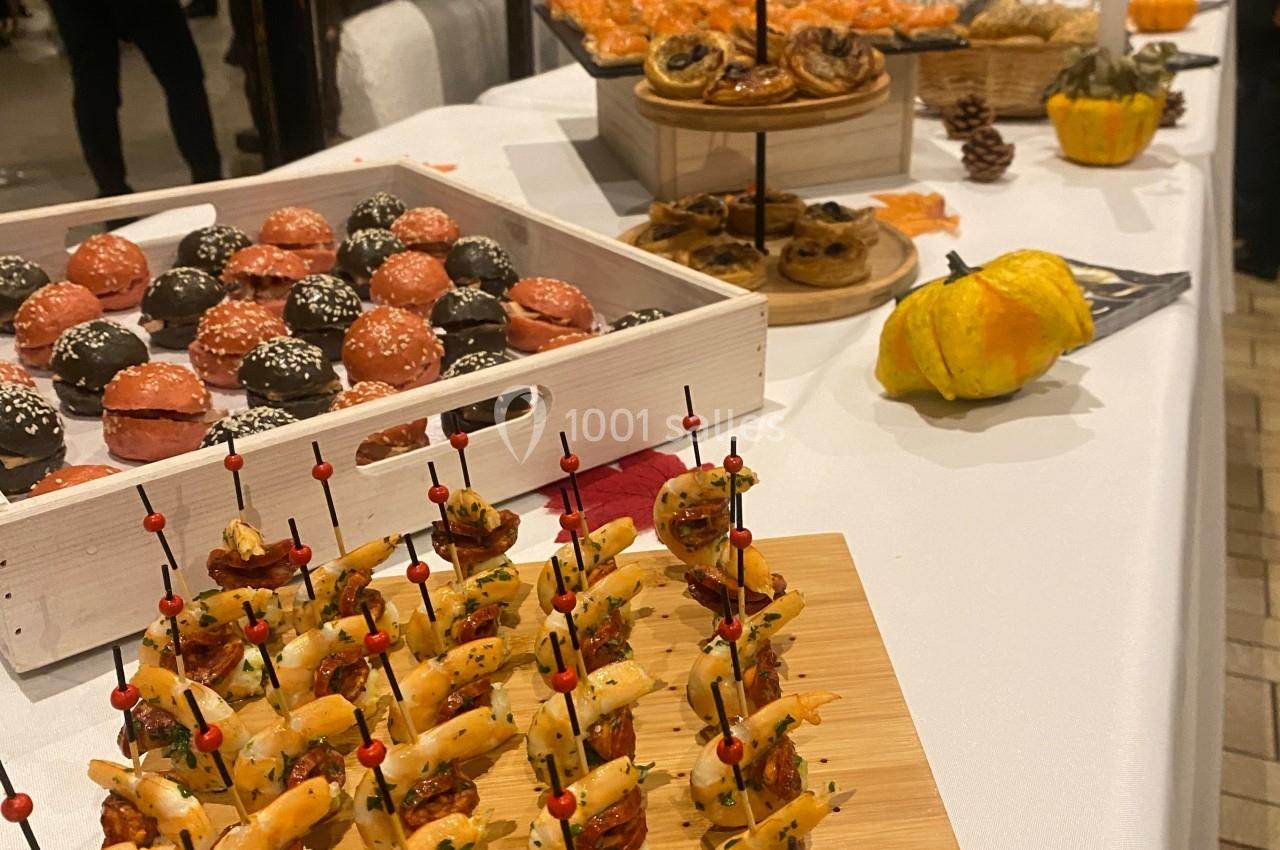 Buffet avec brochettes apéritives, pâtisseries variées et décorations automnales sur une table blanche.