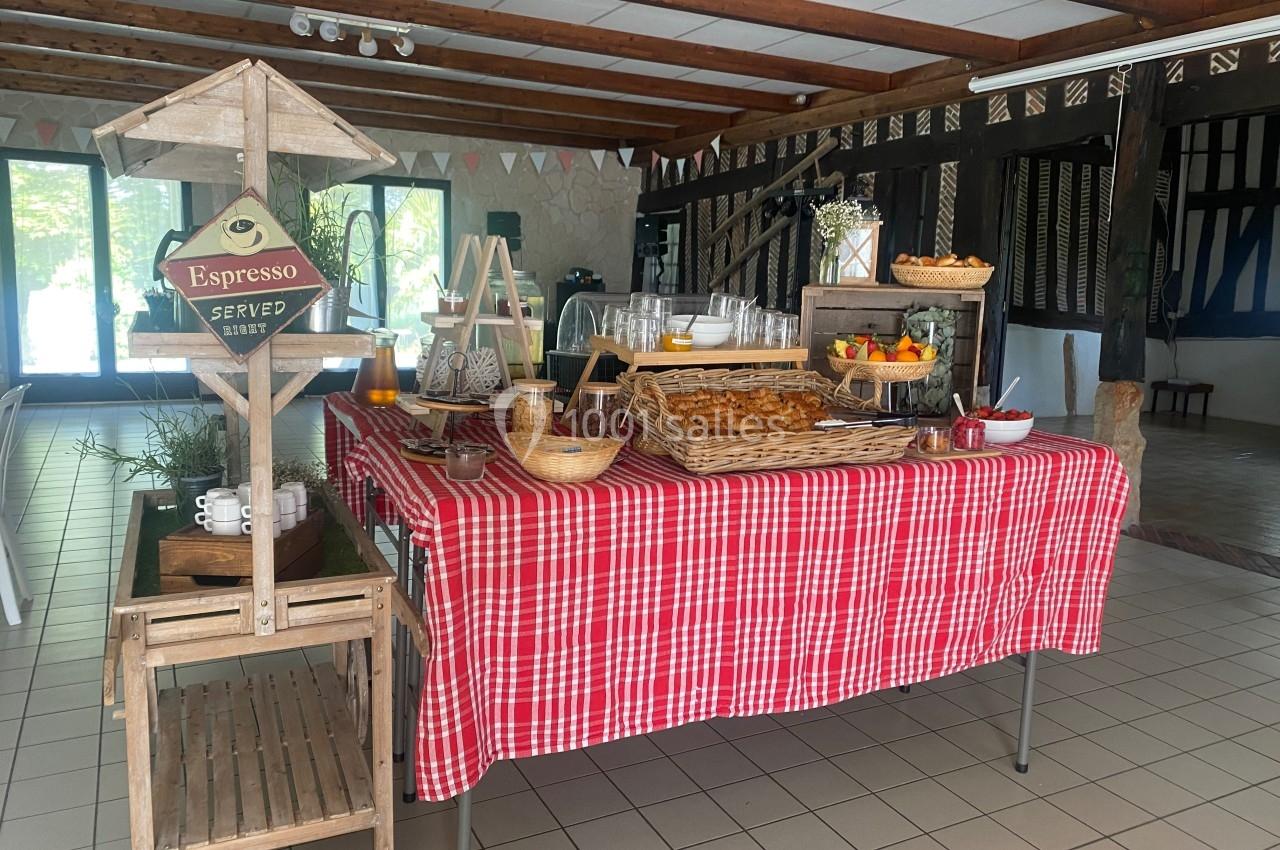 Buffet avec viennoiseries, fruits, jus et café, disposé sur une table recouverte d'une nappe rouge à carreaux.