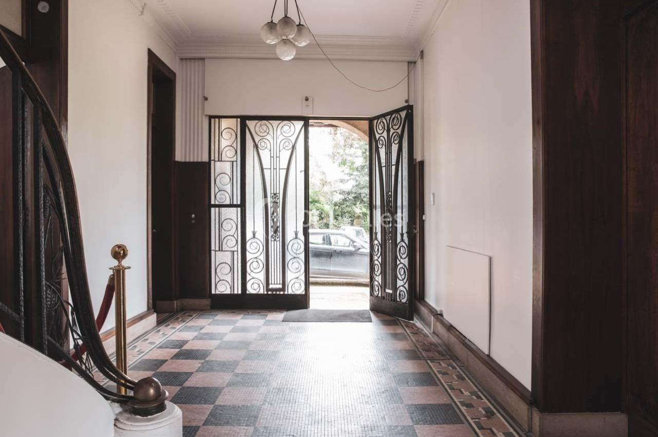 Hall d'entrée lumineux avec sol en carreaux, escalier à gauche et porte-fenêtre ouverte donnant sur l'extérieur.
