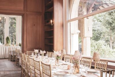 Salle lumineuse décorée pour un événement, avec des tables dressées, des chaises dorées et des fleurs en centre de table.