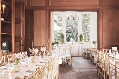 Salle lumineuse décorée pour un événement, avec des tables dressées, des chaises dorées et des fleurs en centre de table.