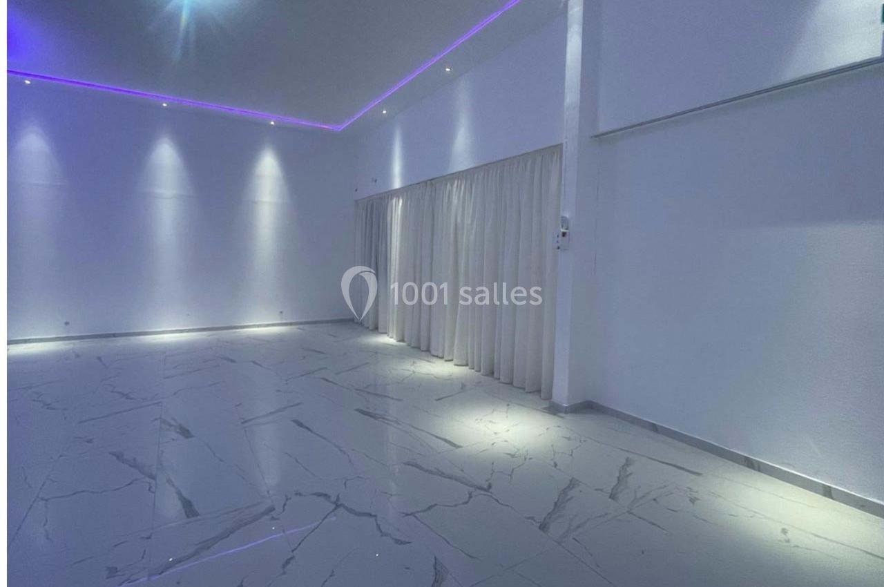 Salle vide avec sol en marbre clair, murs blancs, rideaux fermés et éclairage LED violet au plafond.
