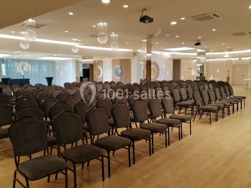 Salle de conférence lumineuse avec rangées de chaises grises alignées sur un sol en bois clair.