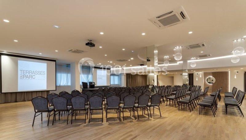 Salle de conférence moderne avec rangées de chaises, écrans de projection et éclairage suspendu.