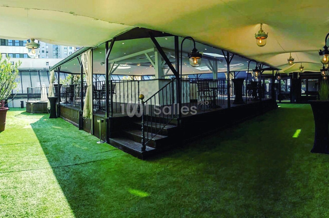 Espace extérieur couvert avec pelouse artificielle, terrasse surélevée et lampes suspendues.