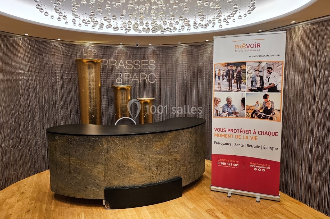Comptoir d'accueil en pierre devant un panneau publicitaire, dans un espace décoré de colonnes dorées et d'un plafond…