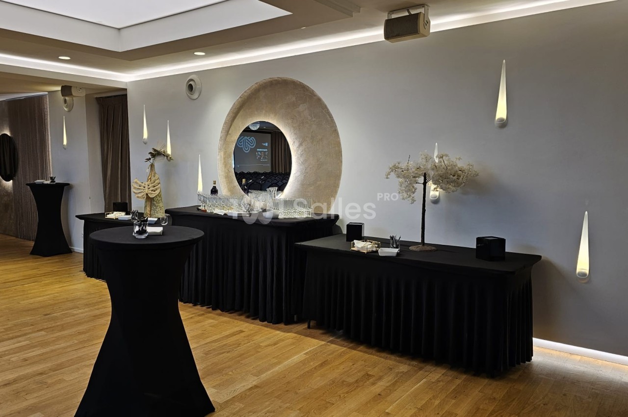 Salle élégante avec tables hautes noires, buffet décoré et éclairage mural moderne sur parquet clair.