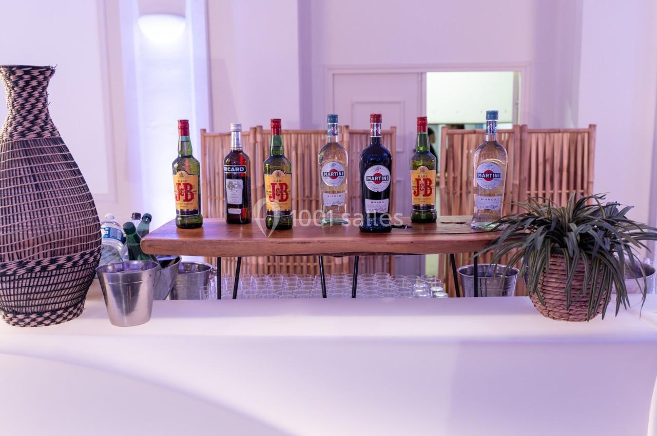 Bouteilles d'alcool variées alignées sur un comptoir en bois, entourées de paniers décoratifs et de plantes.