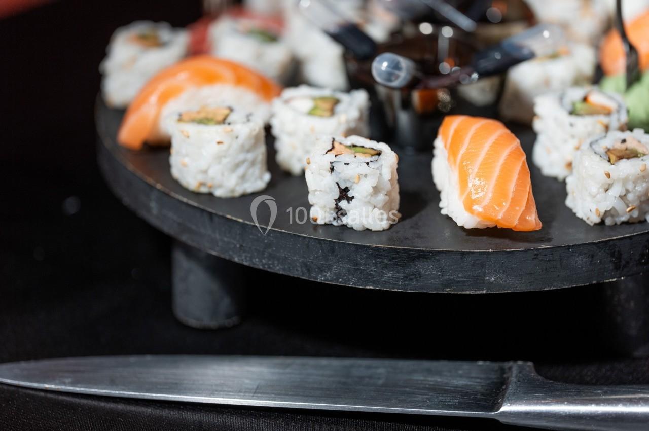 Assortiment de sushis et makis sur un plateau rond avec un couteau en métal au premier plan.