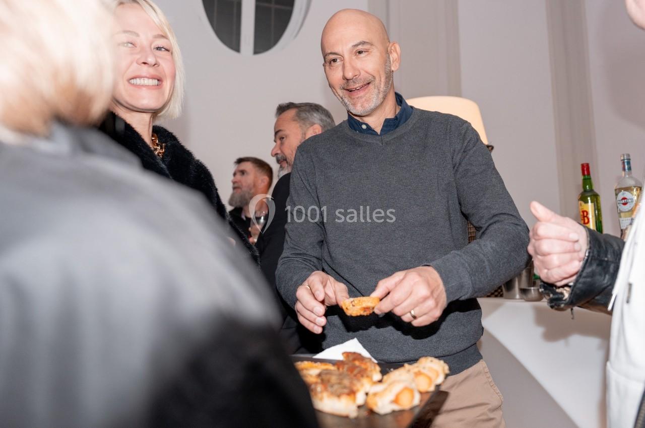 Un homme souriant prend un amuse-bouche sur un plateau lors d'un événement convivial en intérieur.