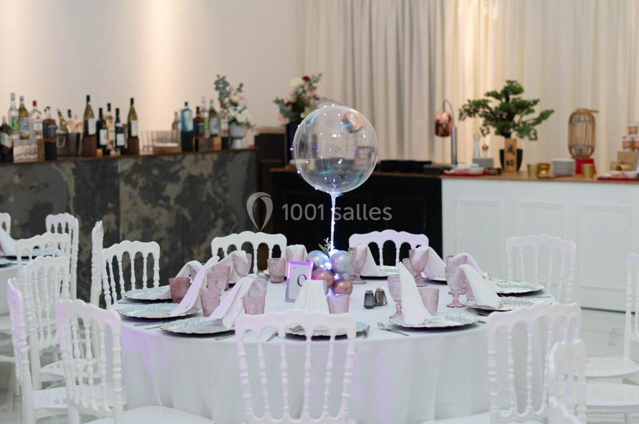 Table décorée pour un événement avec nappes blanches, serviettes roses, ballon transparent et arrière-plan de bar.